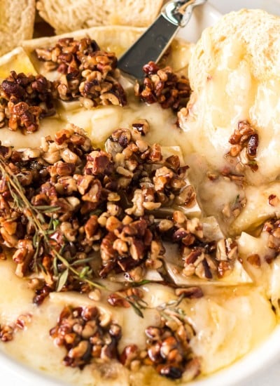 bread and a cheese knife stuck into melty baked brie with pecans and honey