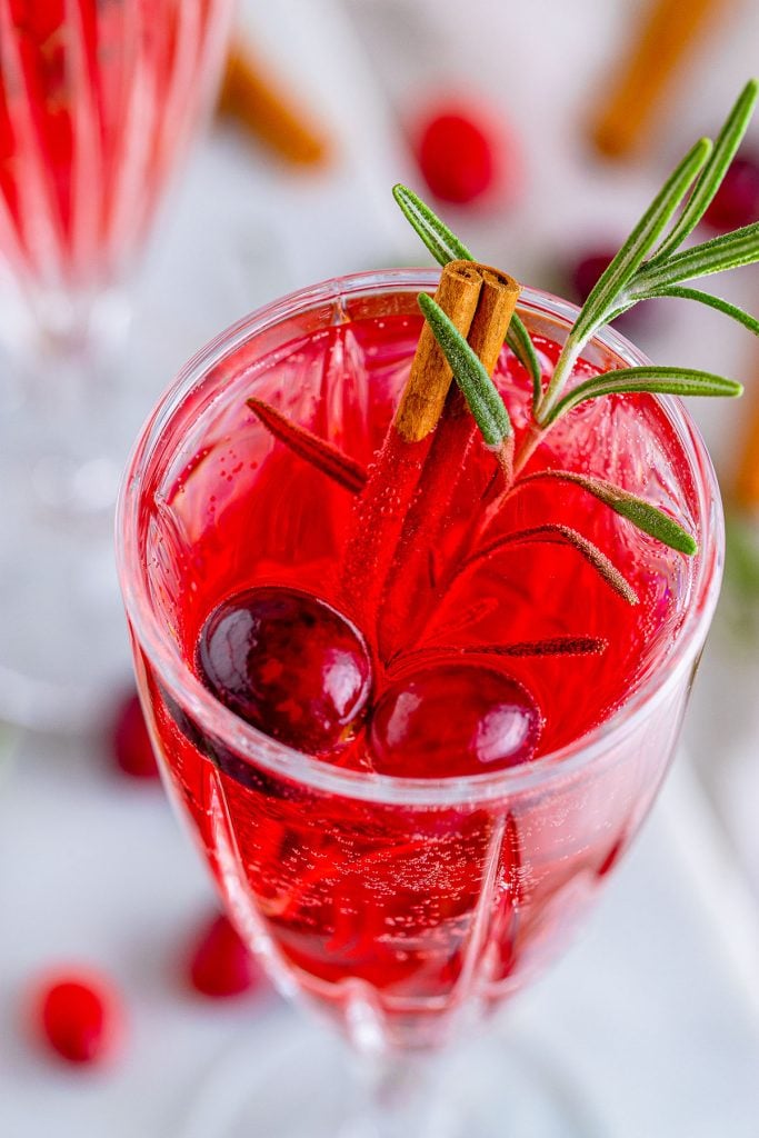 closeup shot of a red christmas cocktail garnished with cranberries and rosemary