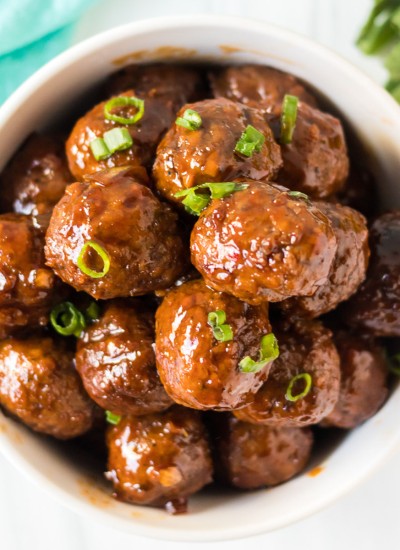overhead shot of honey garlic meatballs in a white bowl sprinkled with green onions