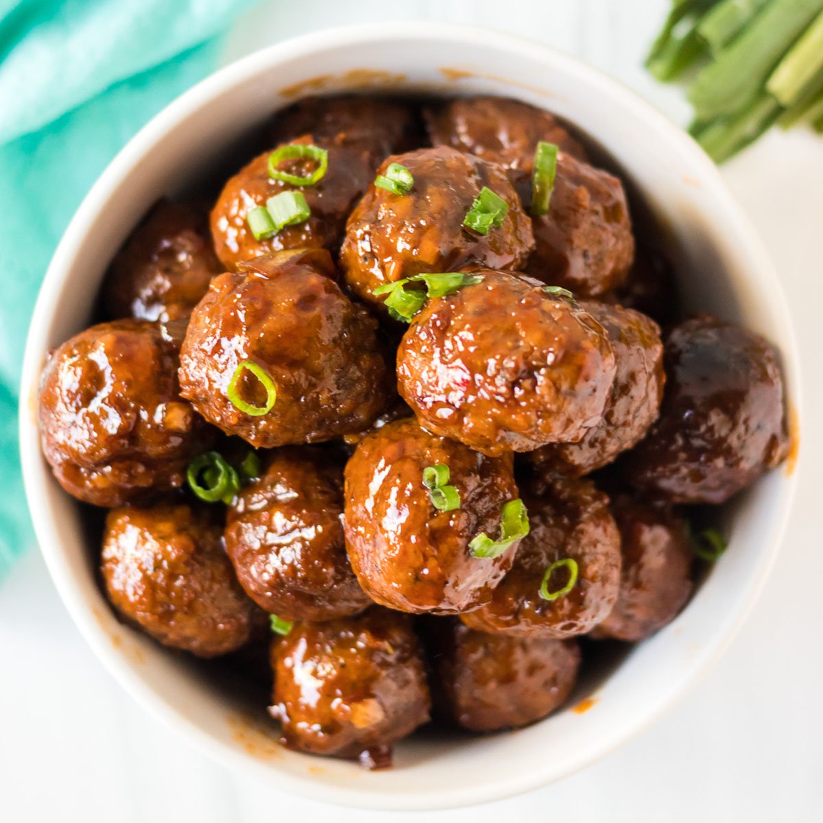 overhead shot of honey garlic meatballs in a white bowl sprinkled with green onions
