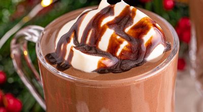 hot chocolate in a glass mug topped with whipped cream and chocolate sauce