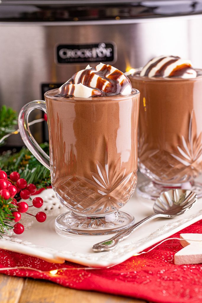 two clear glass mugs filled with hot chocolate and topped with whipped cream and chocolate sauce