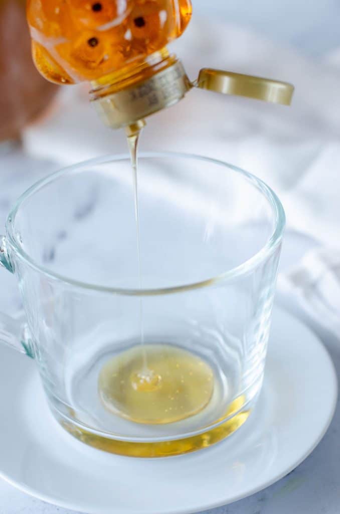 honey pouring into a glass mug.