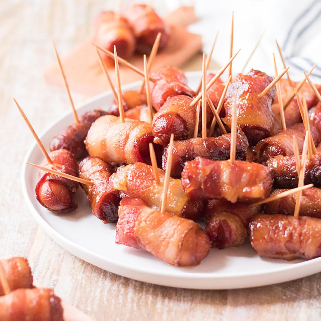 white plate stacked with bacon wrapped smokies held together by toothpicks