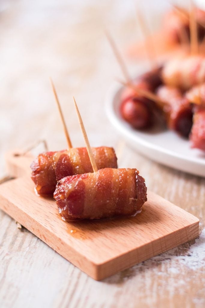 two bacon wrapped little smokies on a wood serving plate