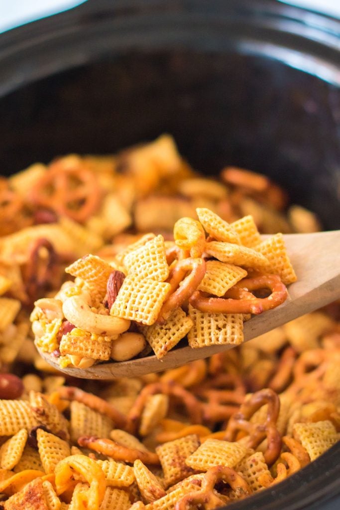 wooden spoon scooping cajun chex mix from a slow cooker