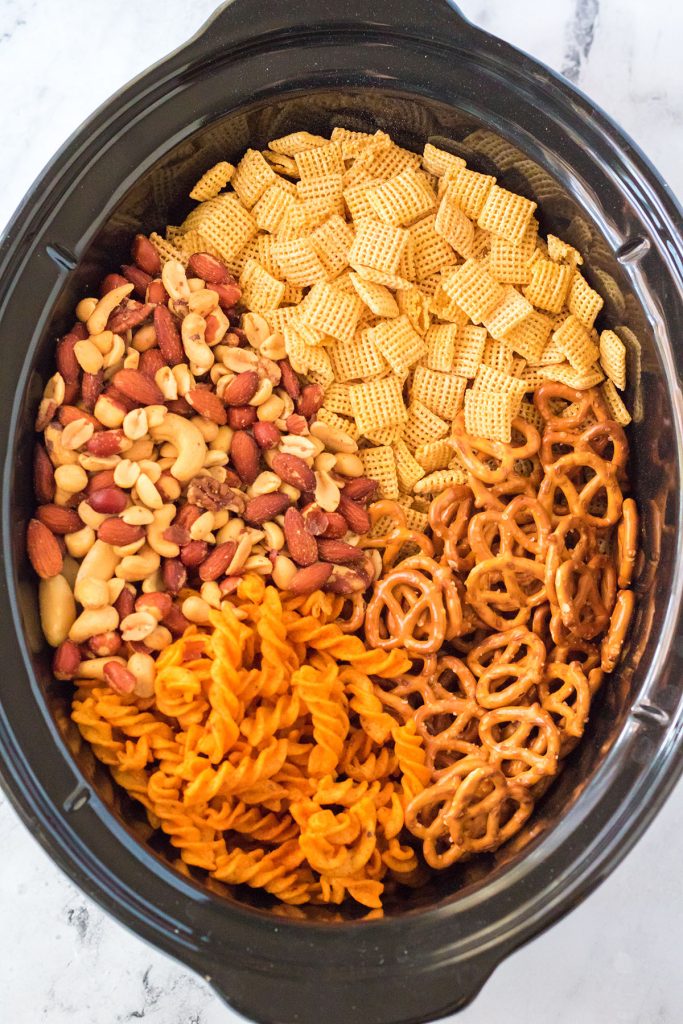 overhead shot of chex cereal, pretzels, and nuts in a slow cooker to make chex mix