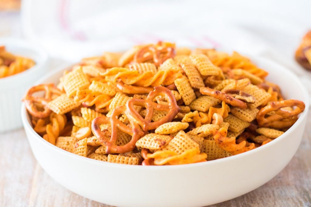 side view of a white bowl filled with cajun chex mix