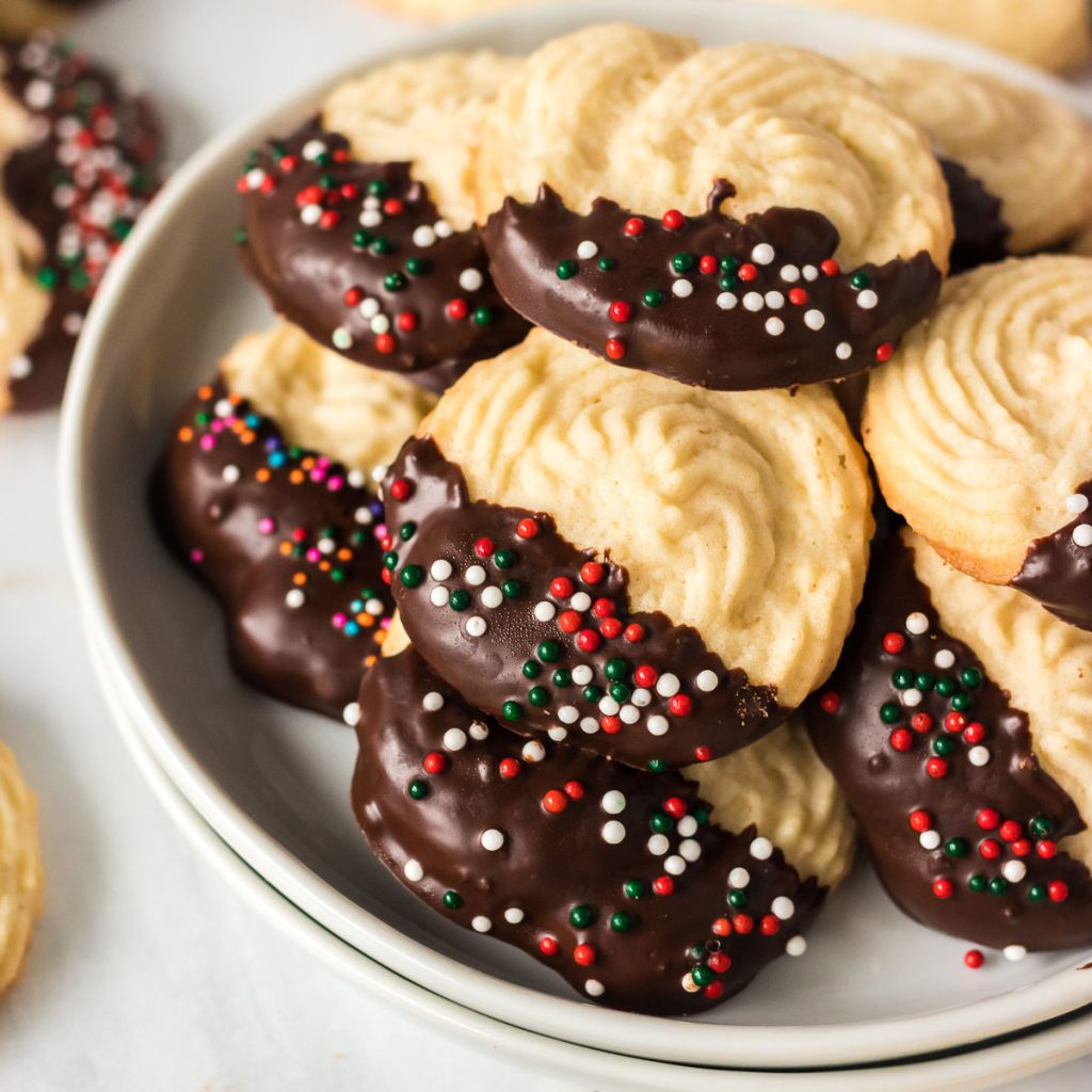 white plate stacked with chocolate dipped butter cookies and holiday sprinkles