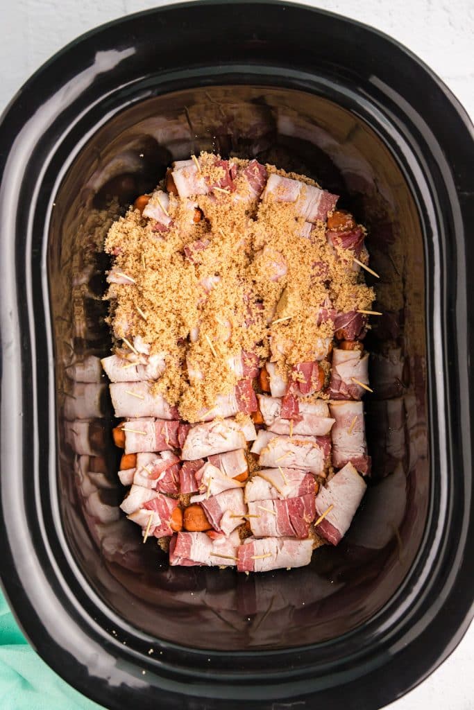 overhead shot of brown sugar sprinkled on bacon wrapped little smokes in a crockpot.