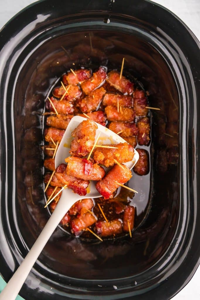 spoon lifting bacon wrapped lil smokies from a slow cooker.