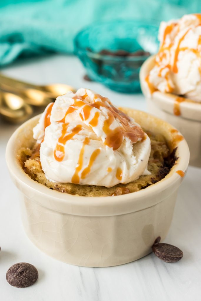 a microwave chocolate chip cookie topped with vanilla ice cream & caramel in a ramekin