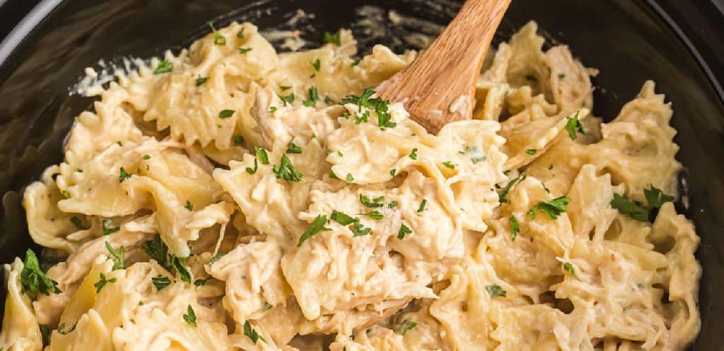 wooden spoon scooping creamy italian chicken from a crockpot.