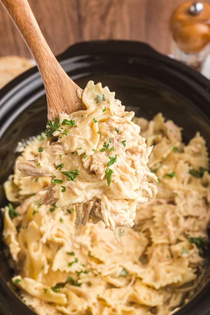 wooden spoon lifting a scoop of creamy italian chicken from a crockpot.