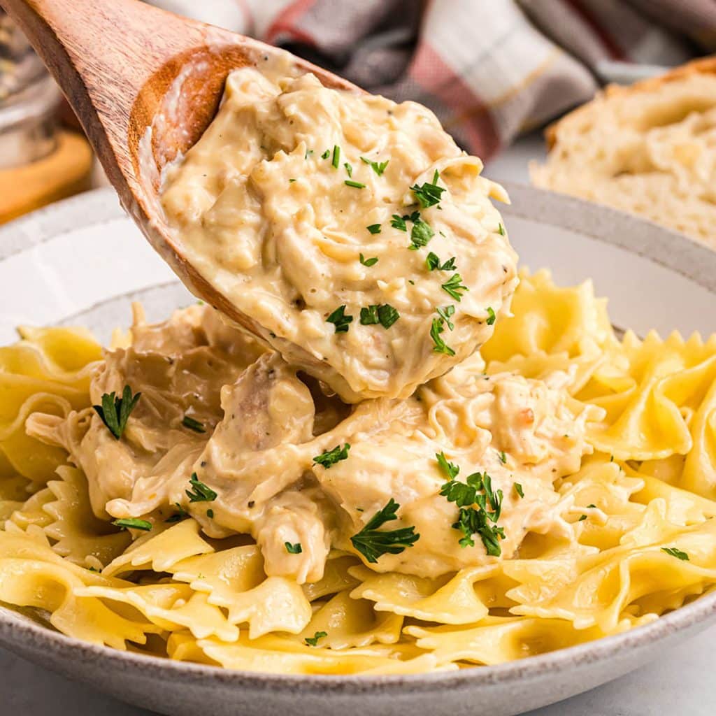 spoon scooping creamy italian chicken onto a bed of bowtie noodles.