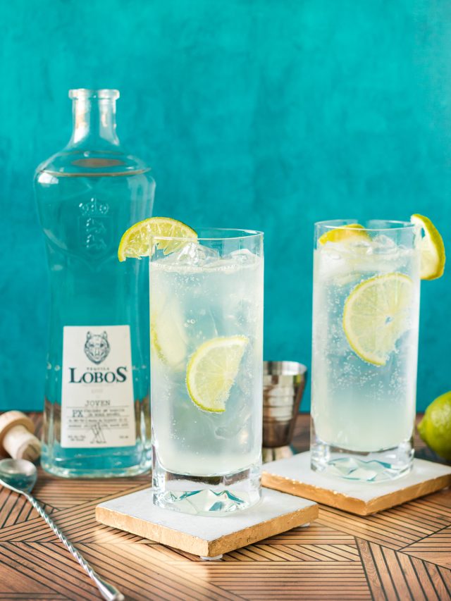 two cocktails with lime wedges next to a bottle of lobos tequila