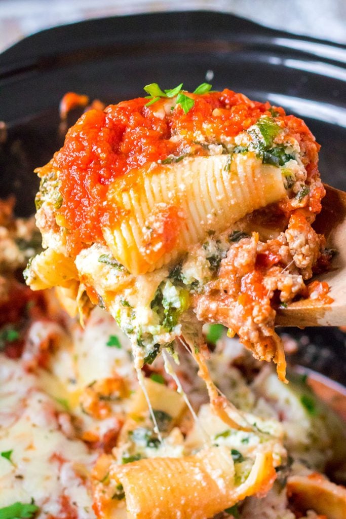 a cheesy, saucy, stuffed shell being lifted from the slow cooker.