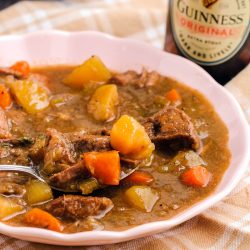 bowl of beef stew next to a bottle of guinness beer.
