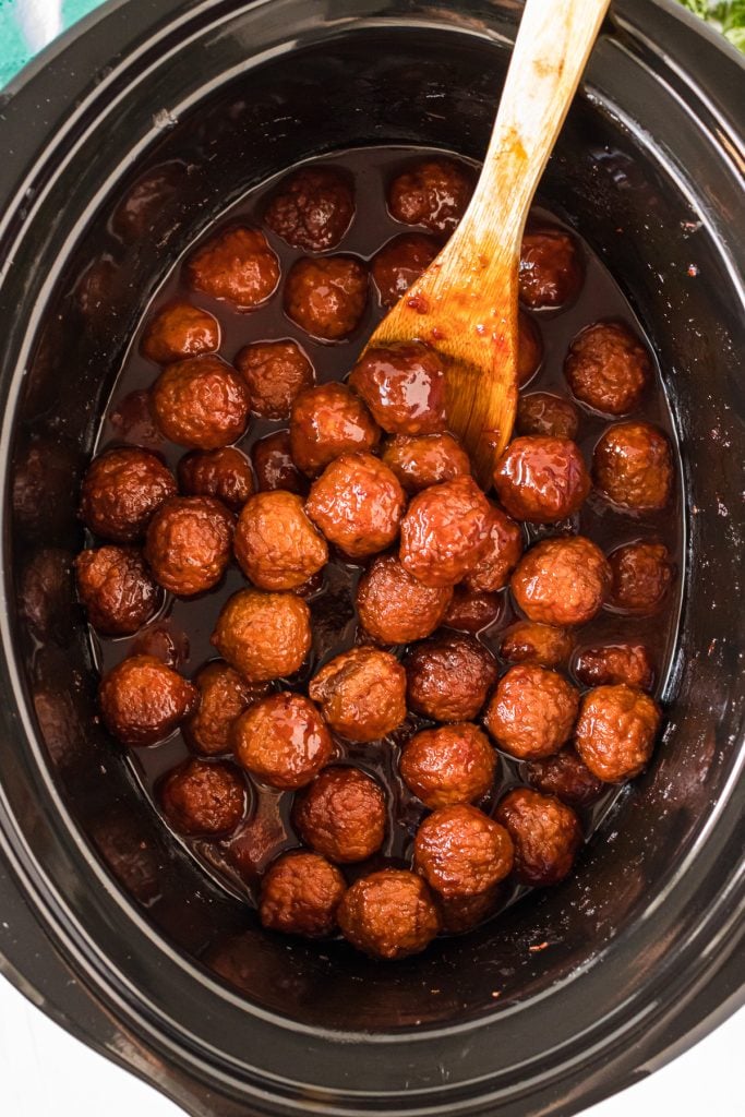 overhead shot of meatballs in a slow cooker with a wooden spoon.
