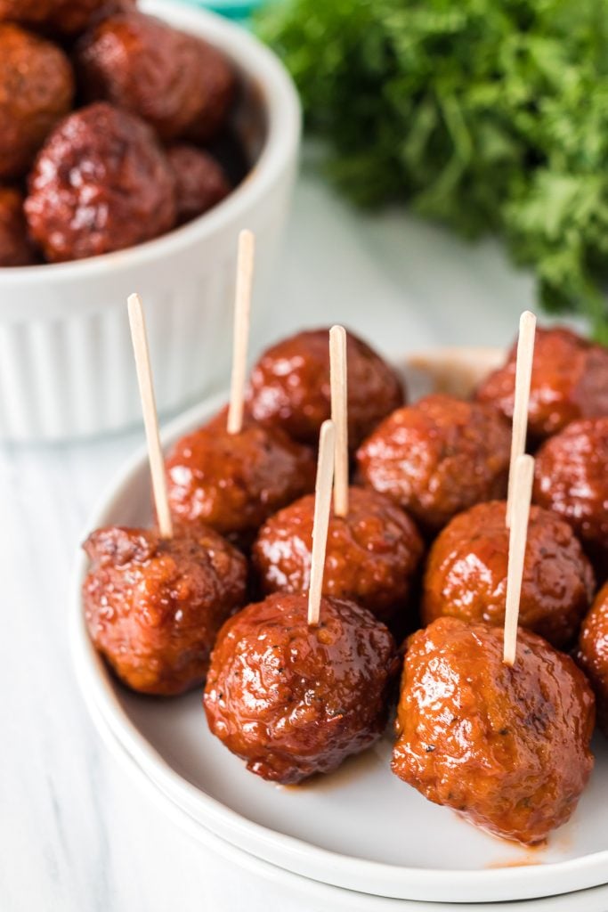 grape jelly meatballs stuck with toothpicks on a white plate.