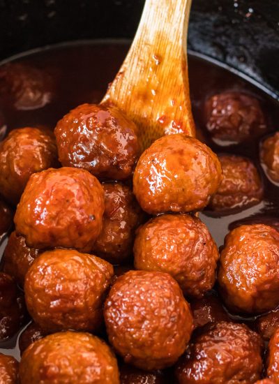 wooden spoon scooping grape jelly meatballs from a crockpot.