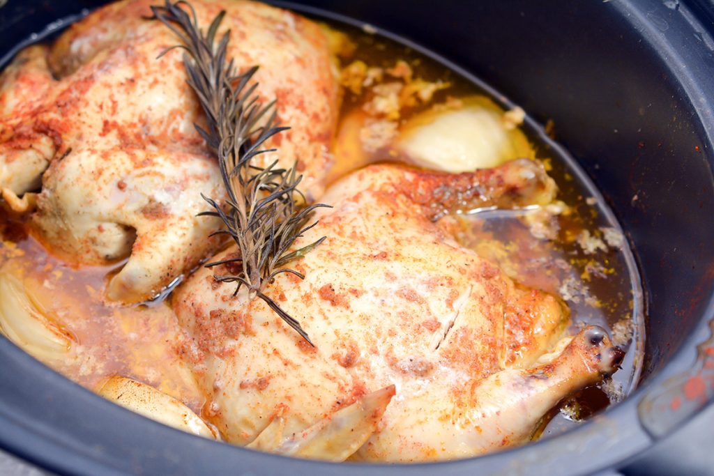 two cornish hens in a crockpot topped with rosemary sprig.