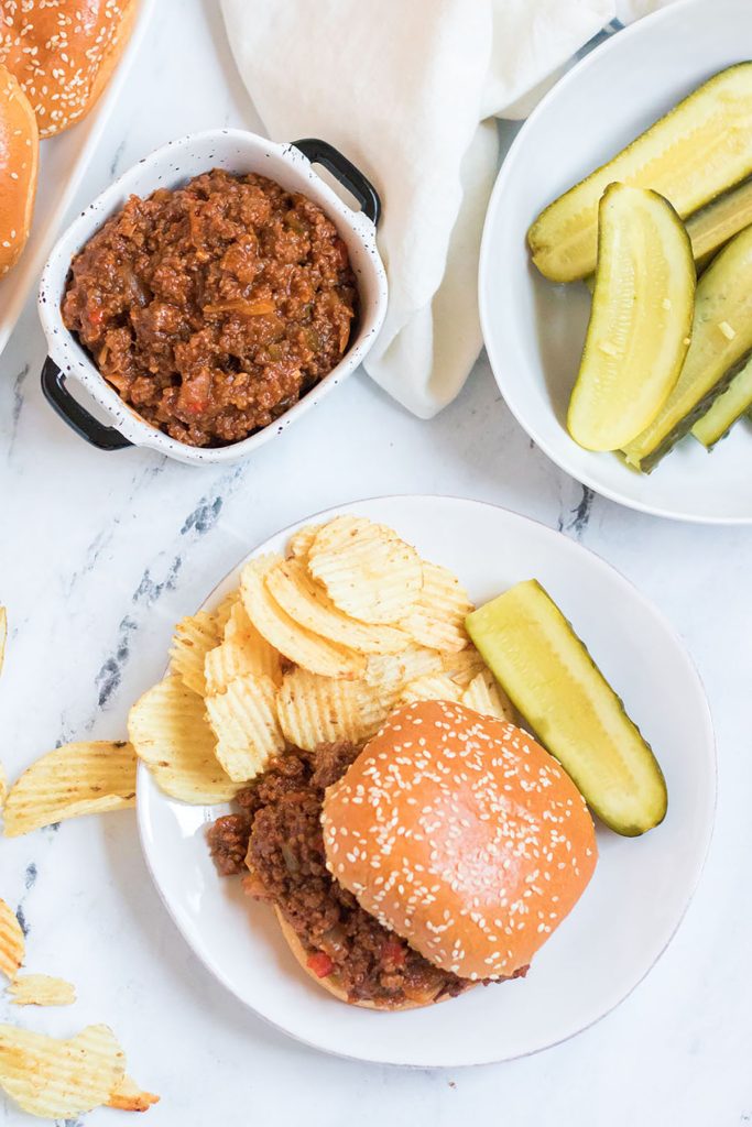 overhead shot of plated sloppy joe with potato chips and pickles.