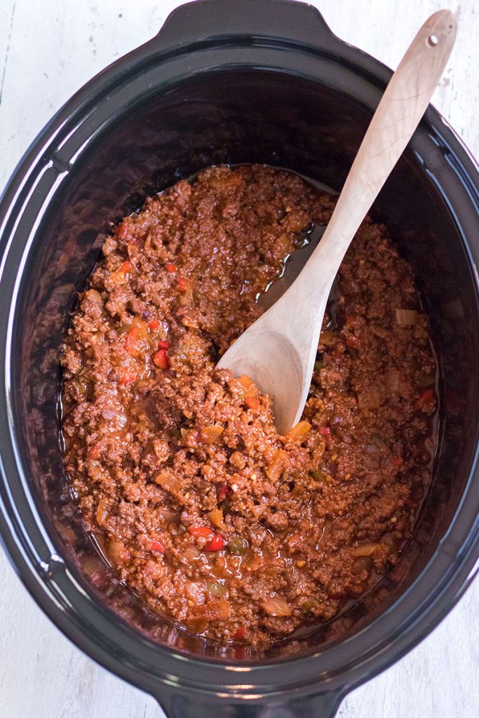 wooden spoon scooping sloppy joe meat mixture from a slow cooker.