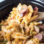 wooden spoon scooping cajun chicken pasta from a slow cooker.