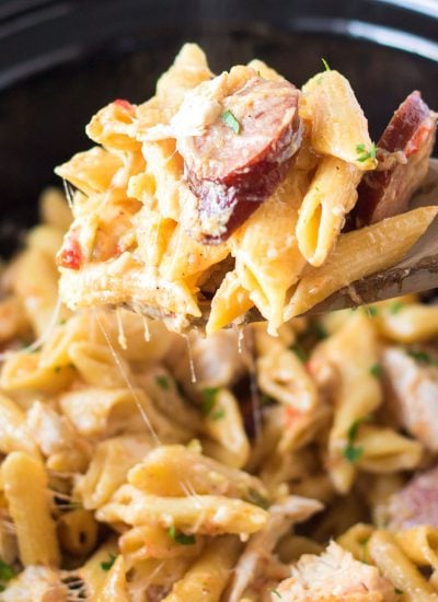wooden spoon scooping cajun chicken pasta from a slow cooker.