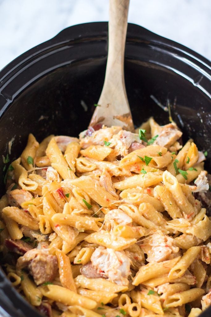 wooden spoon scooping penne pasta from a crockpot.