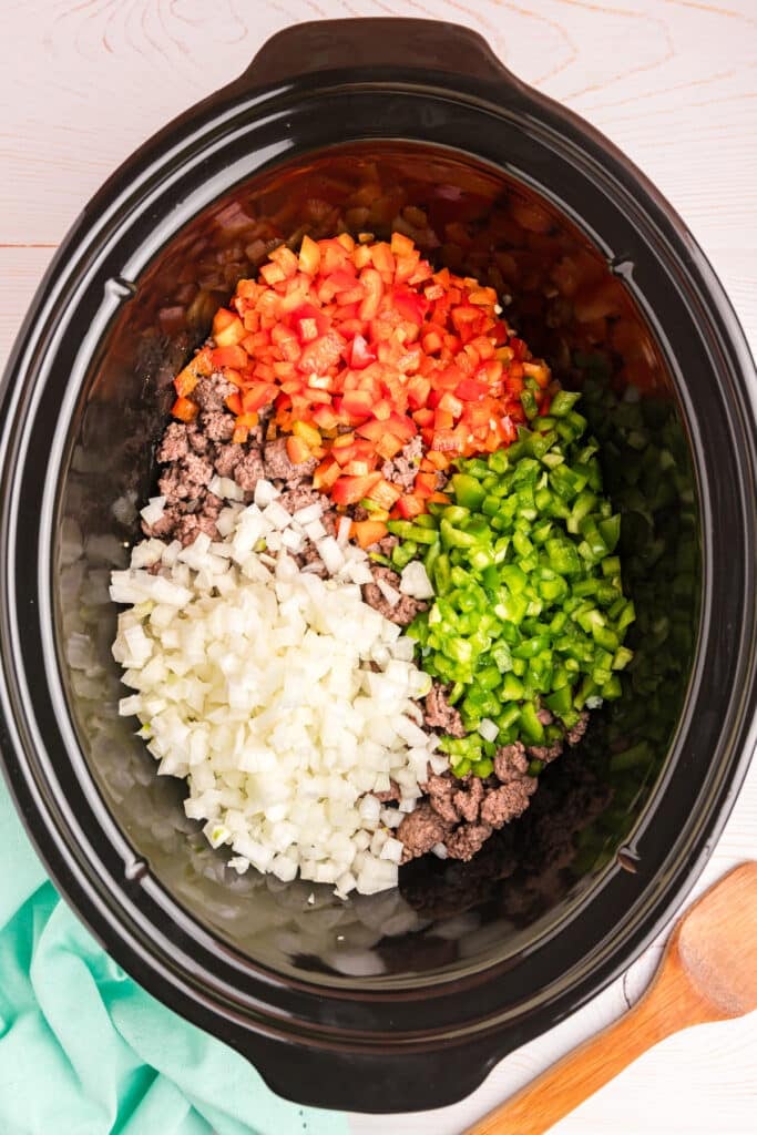 overhead shot of diced onions and bell peppers in a black crockpot.