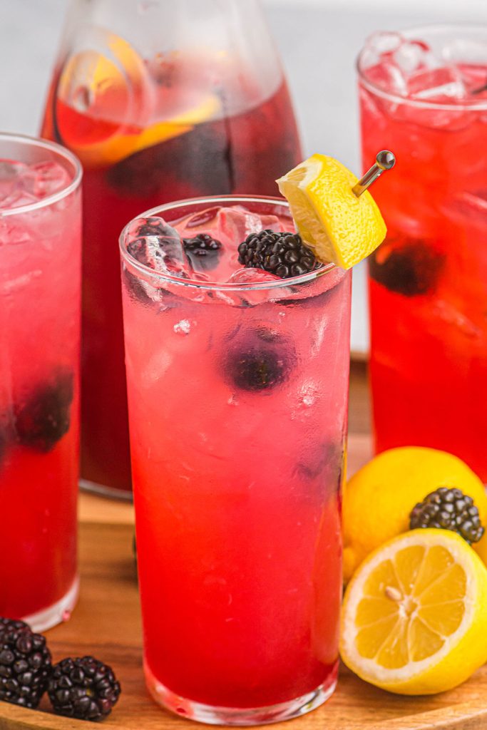 tall glasses of pink lemonade garnished with blackberries and lemon.