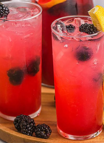 try of glasses filled with blackberry lemonade surrounded by lemons.