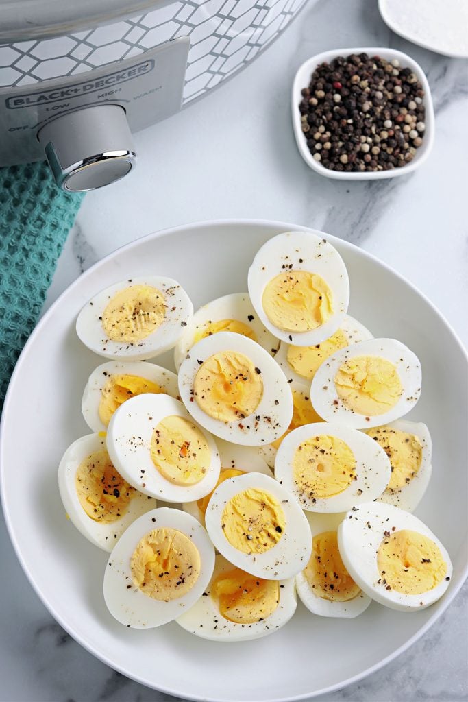 overhead shot of peppered, sliced hard boiled eggs next to a crockpot.