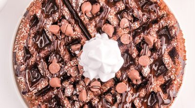 overhead shot of chocolate waffle with chocolate sauce, chocolate chips, and whipped cream.