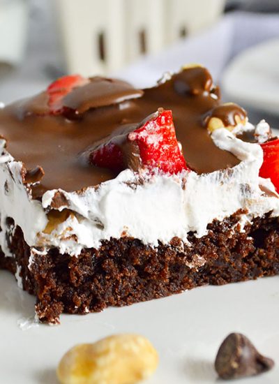 plate of layered strawberry brownie delight surrounded by peanuts and chocolate chips.
