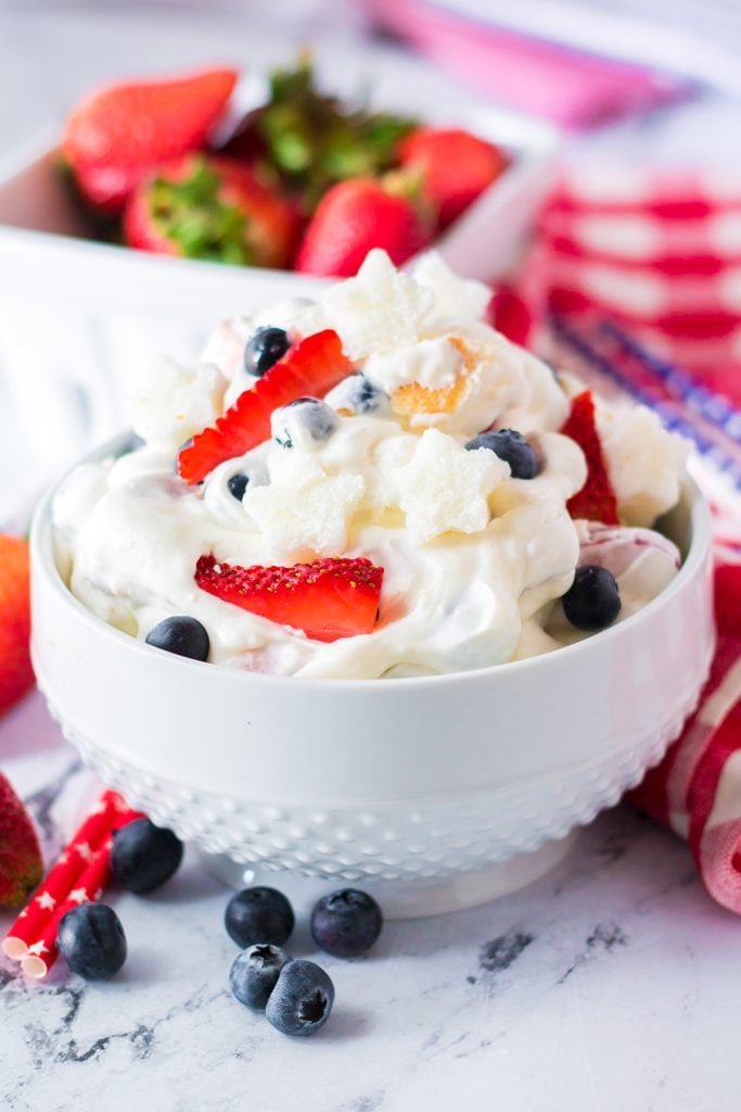 closeup of berry cheesecake fluff in a white bowl surrounded by berries.