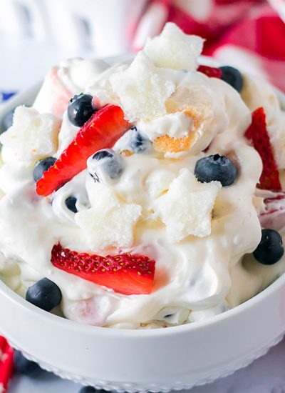 closeup of berry cheesecake fluff salad in a white bowl topped with berries.
