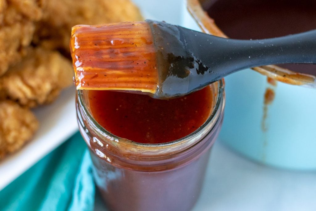 jar of bbq sauce with a brush resting on top.