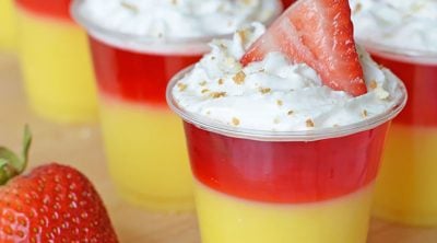 layered strawberry shortcake jello shot topped with whipped cream, nilla wafer crumbs, and strawberry slice.
