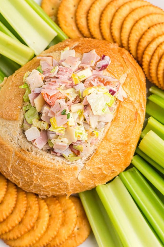 overhead shot of italian hoagie dip in a bread bowl surrounded by crackers & celery.