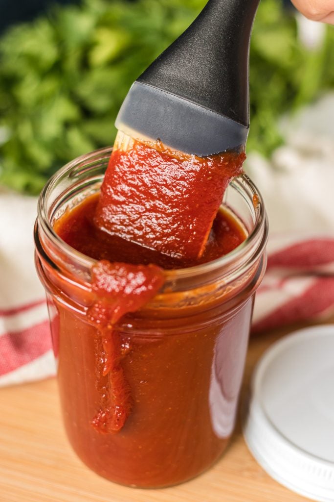 saucing basting brush being lifted from a mason jar of bbq sauce.