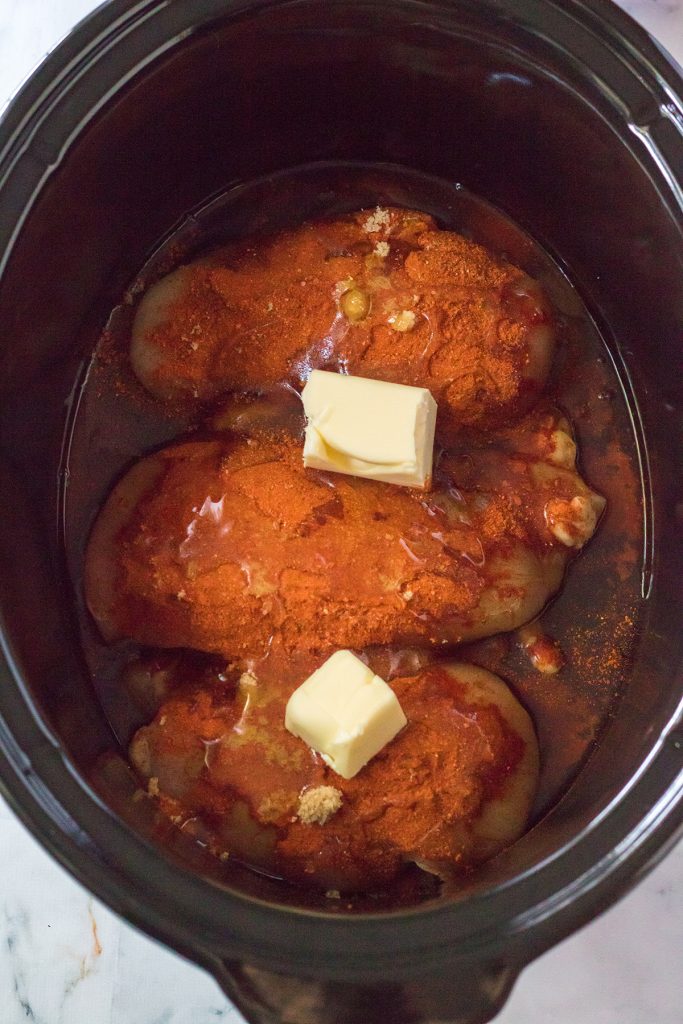 overhead shot of chicken breasts in a slow cooker topped with butter.