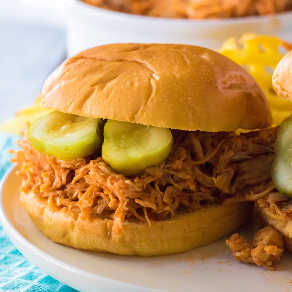 hot honey shredded chicken sandwich on a brioche bun topped with pickles. 