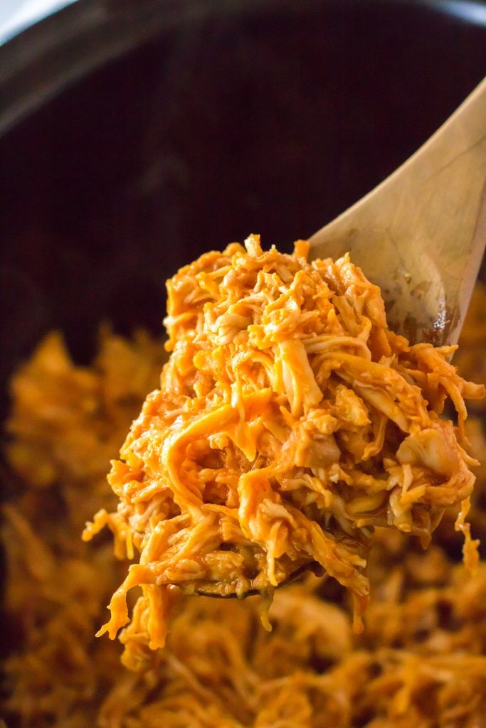 wooden spoon scooping pulled chicken from a slow cooker.