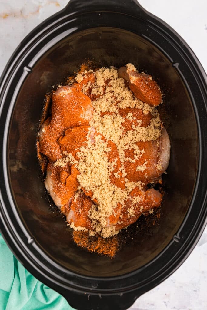 overhead shot of raw chicken and brown sugar in a crockpot.