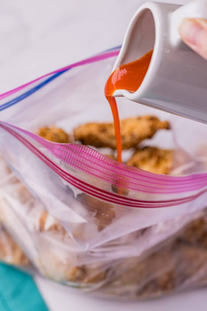 buffalo sauce pouring into a bag of fried chicken.