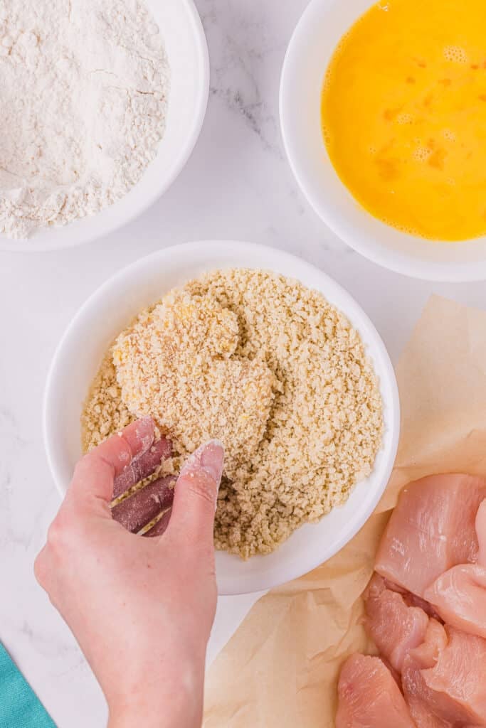 hand dipping chicken into panko breadcrumbs.