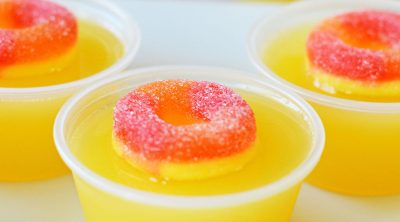 closeup of a fuzzy navel jello shot topped with a peach ring candy.